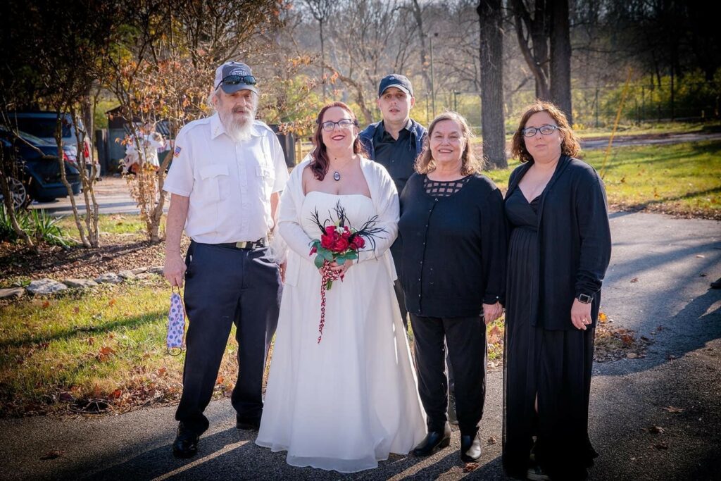 5 people outside surrounding a woman in a wedding dress.