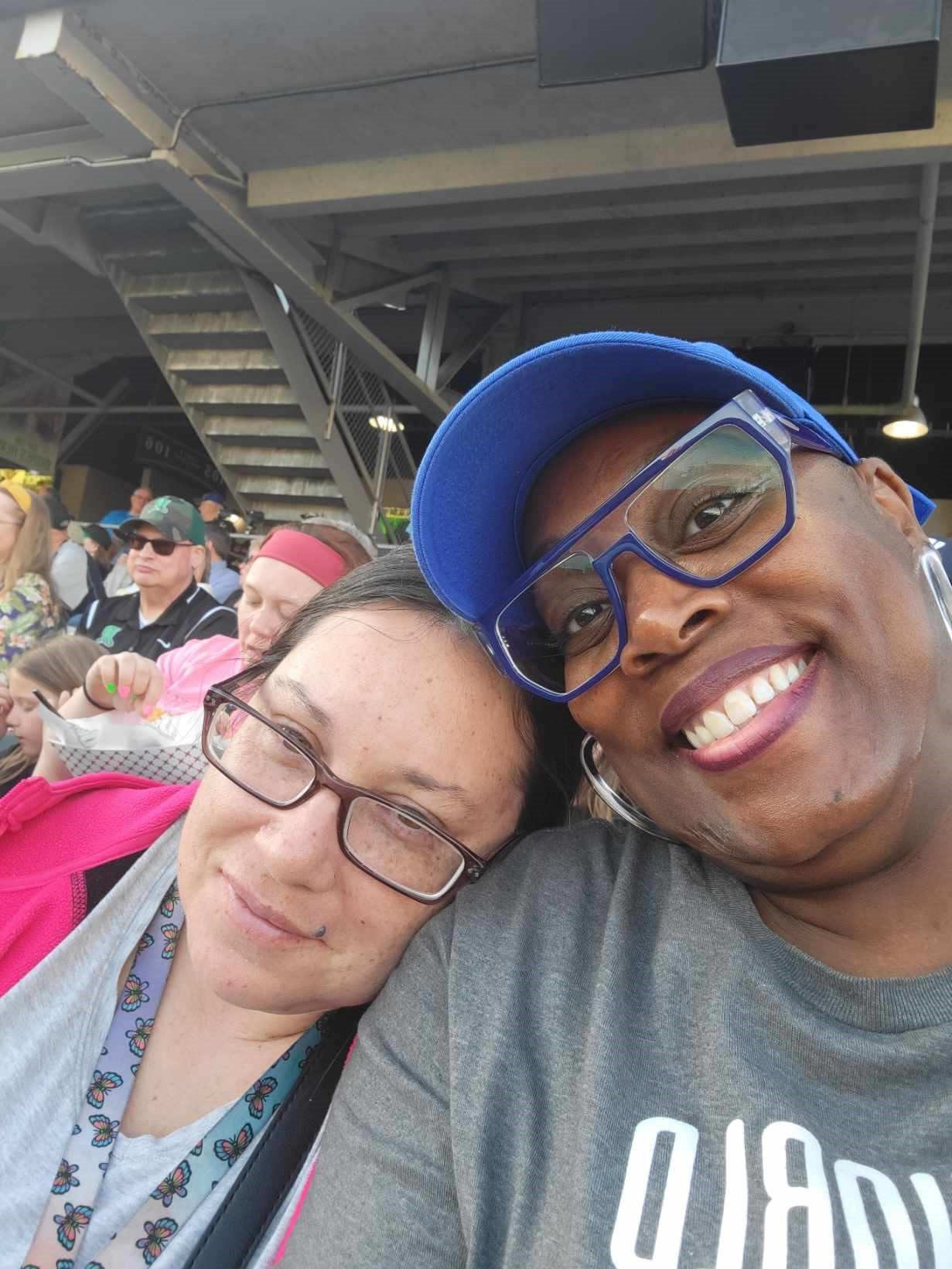 Two women outside at a baseball game smiling side by side