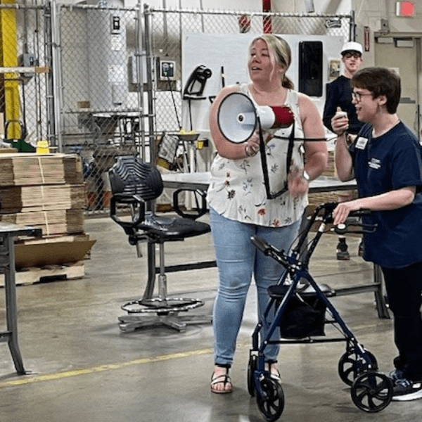 A photo of a woman with a walker and a megaphone standing next time a woman indoors.