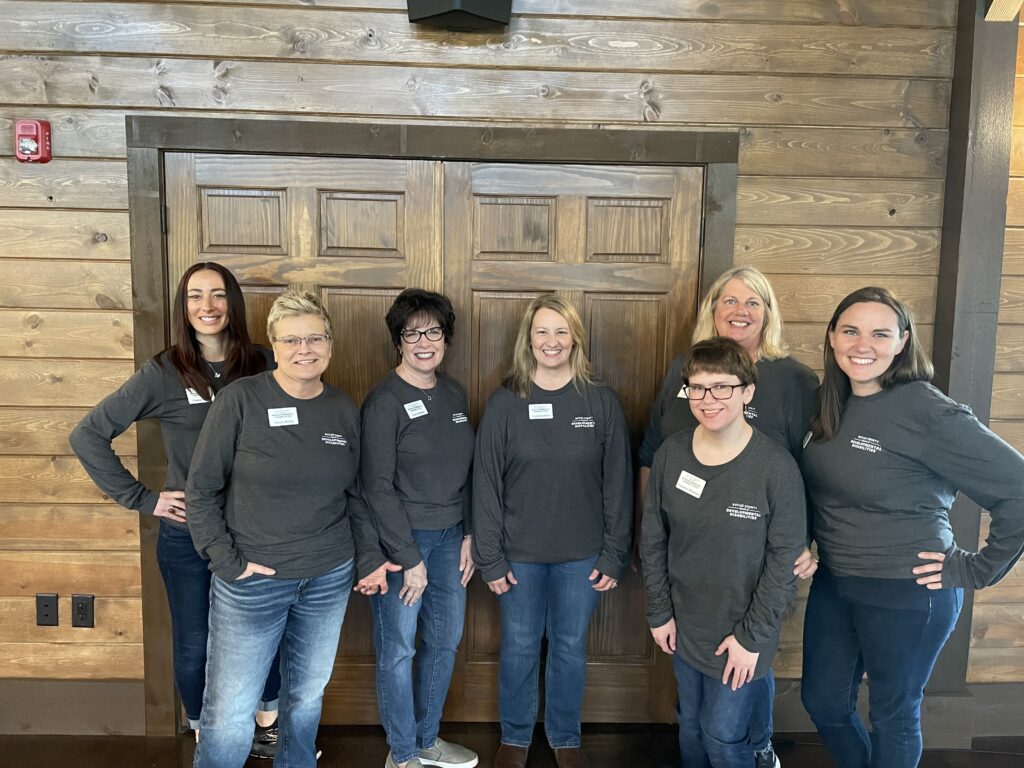 A group of women standing in front of a wooden wall indoors